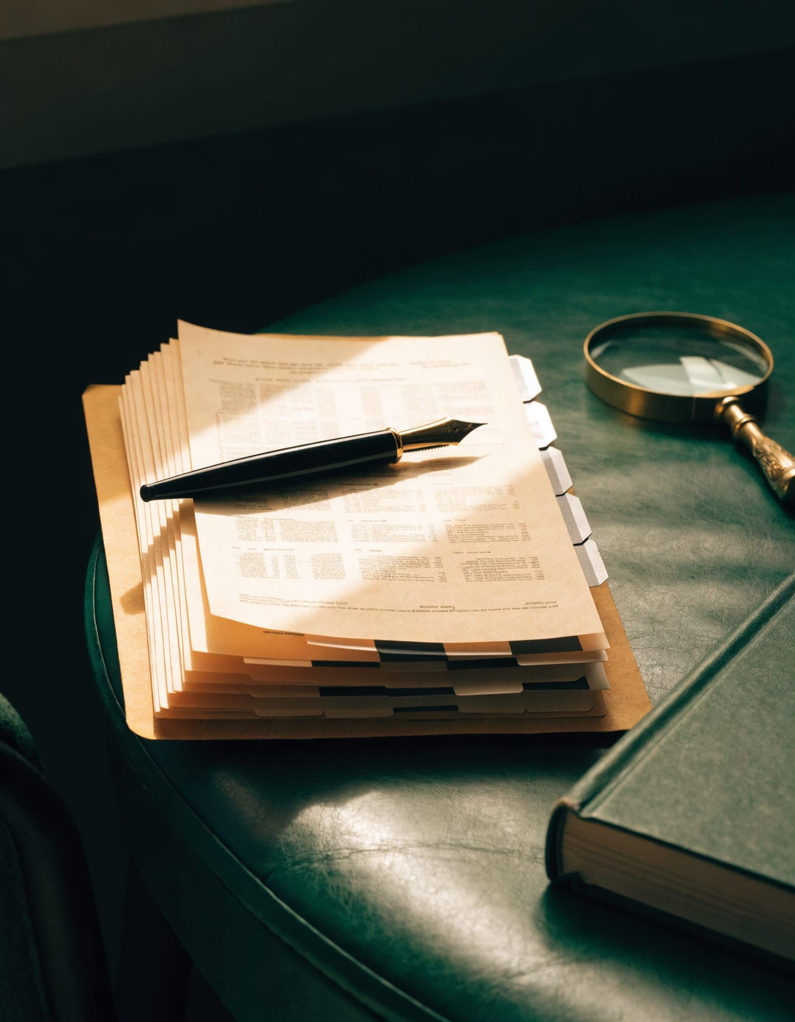 A credit file open on a green leather desk: tabbed statements, a fountain pen, a brass magnifier and a closed ledger.