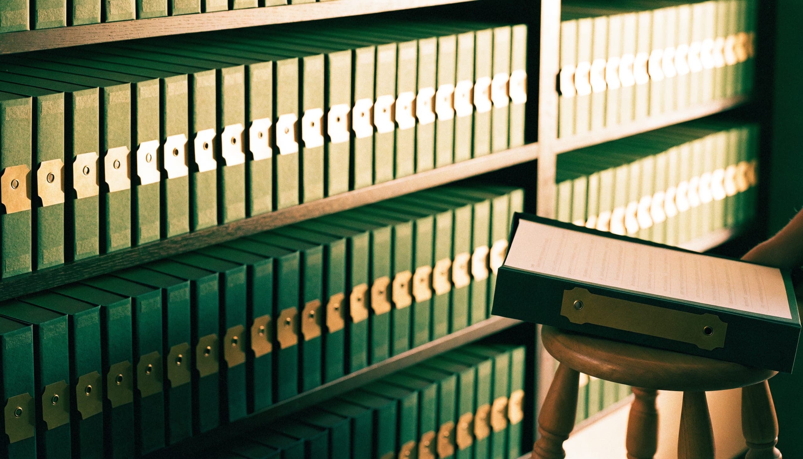 Shelves of matching cloth-bound client binders, one pulled out and lying open on a wooden stool.