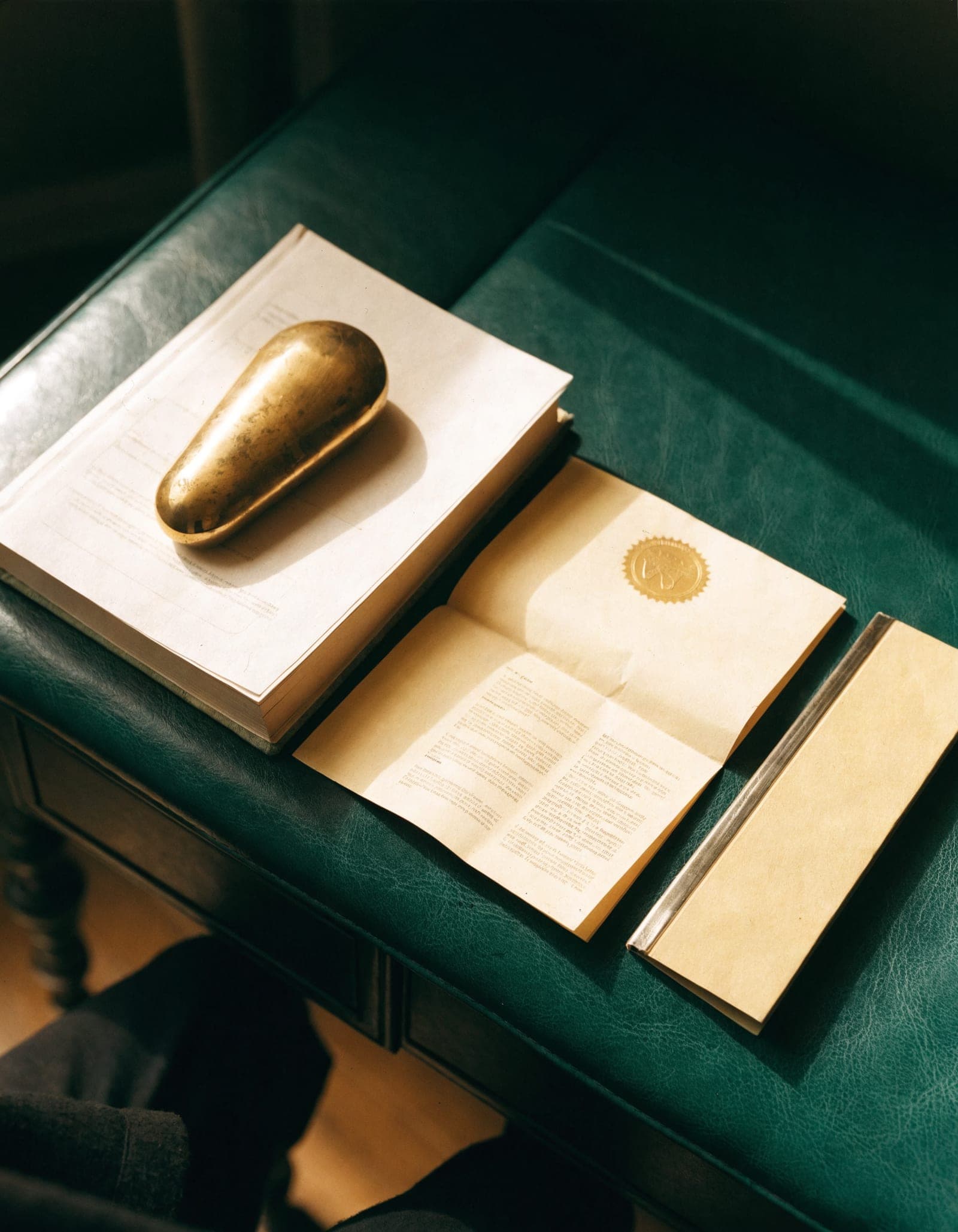 A ledger, a sealed loan agreement and a policy binder arranged on a green leather desk, with a brass paperweight.